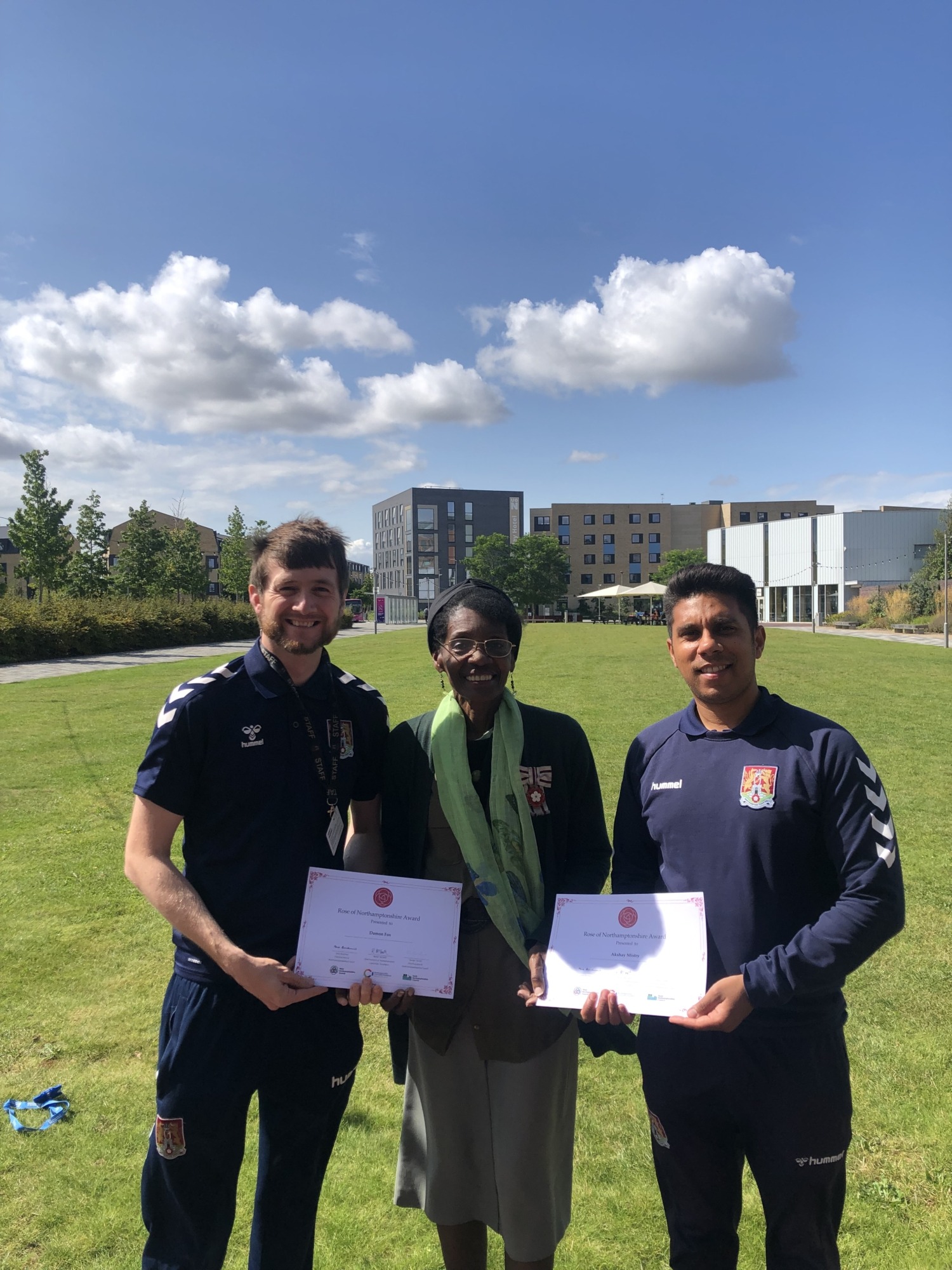 Two members of staff from Northampton Town Football Community Trust stand with VLL Morcea Walker with their Rose of Northamptonshire Award certificates
