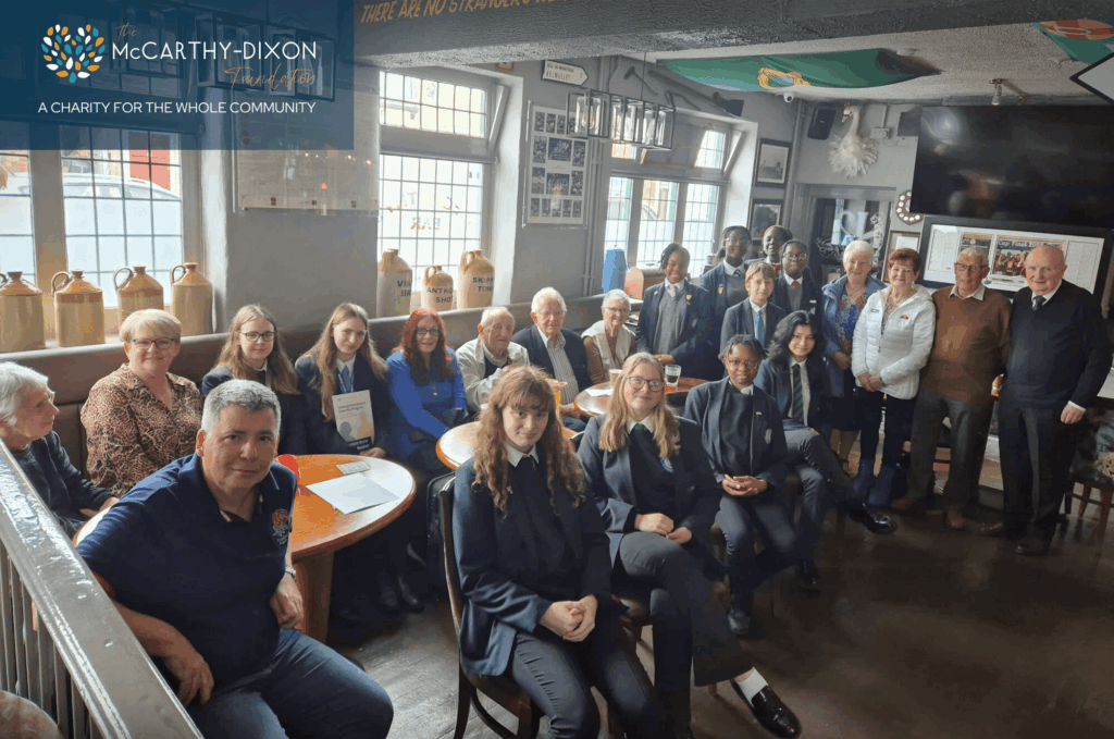 Group of students and older individuals sat together facing the camera